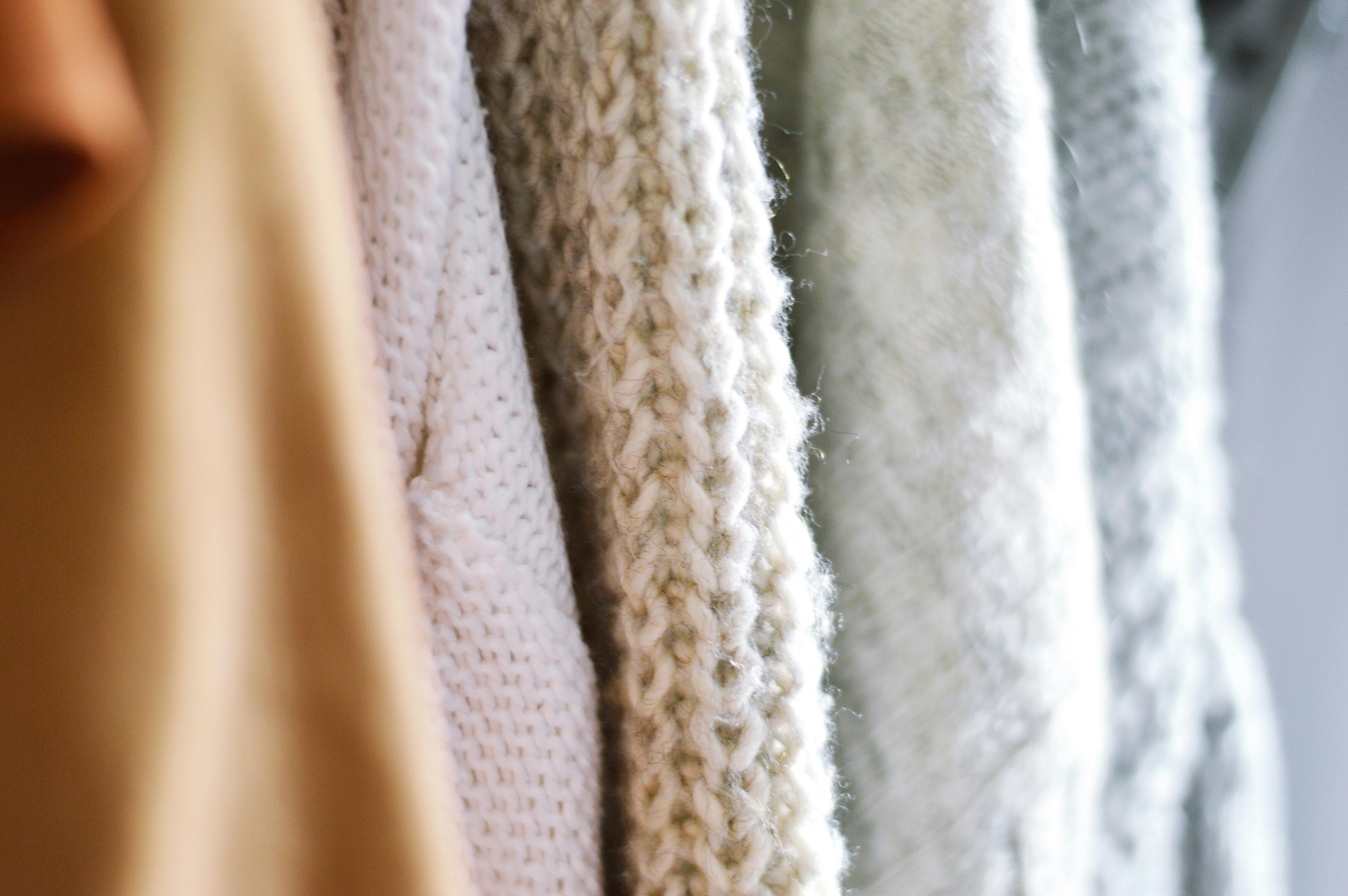 Close-up view of a warm, textured knit sweaters in soft beige and white tones, showcasing intricate weaving and knitting patterns and cozy materials.